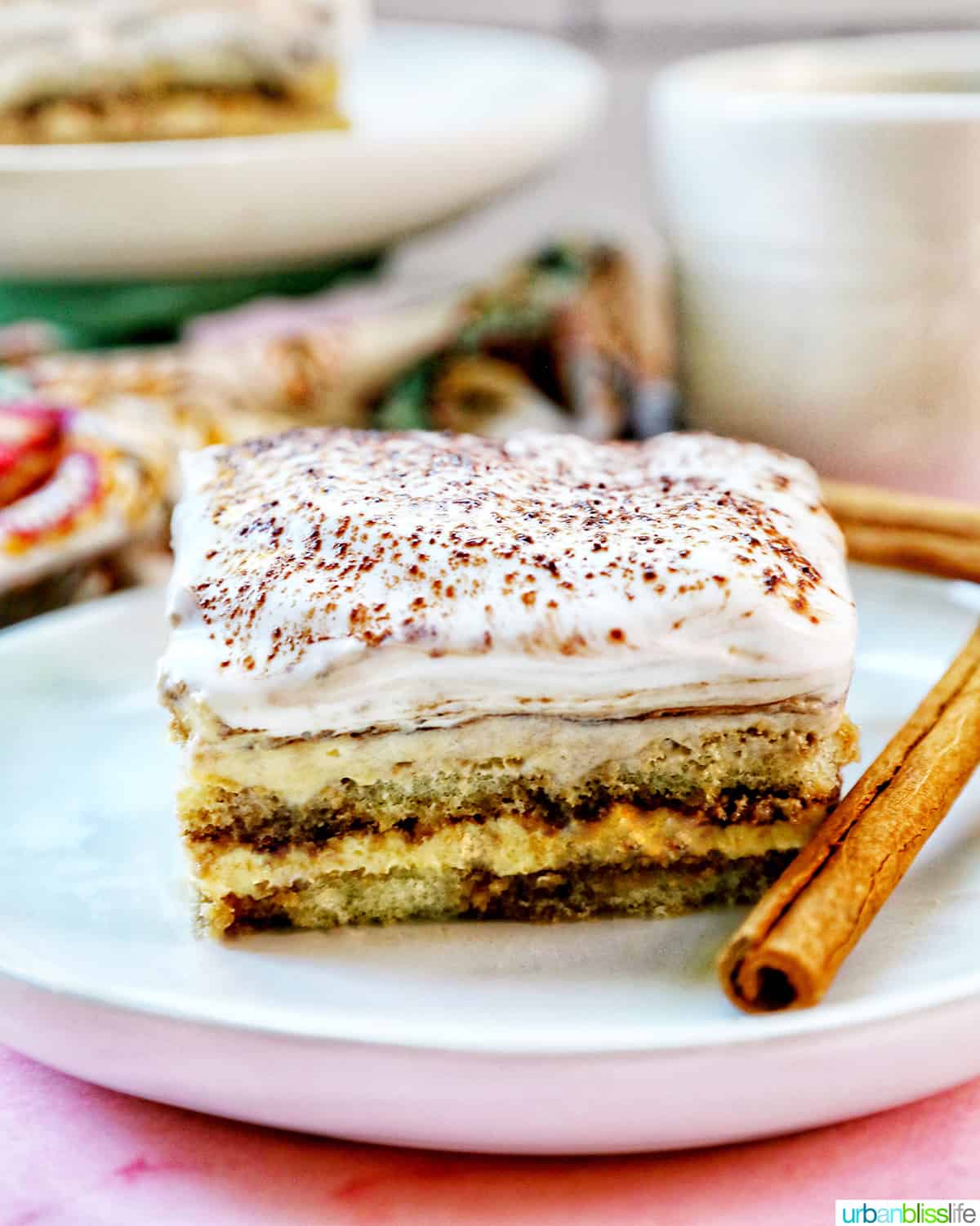slice of dairy free tiramisu dessert on a white plate with cup of coffee behind it.