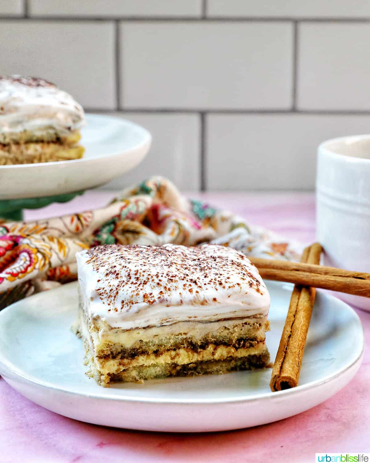 slice of dairy free tiramisu dessert on a white plate with cup of coffee behind it.