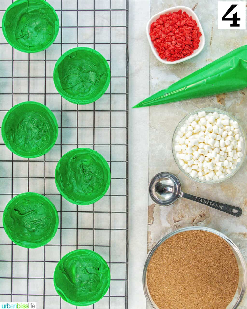 green halves of Grinch hot cocoa bombs with frosting, marshmallows, hot cocoa mix, and red heart sprinkles.