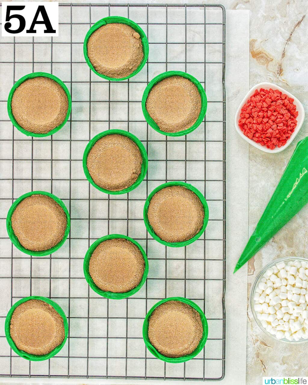 green halves of Grinch hot cocoa bombs with frosting, marshmallows, hot cocoa mix, and red heart sprinkles.