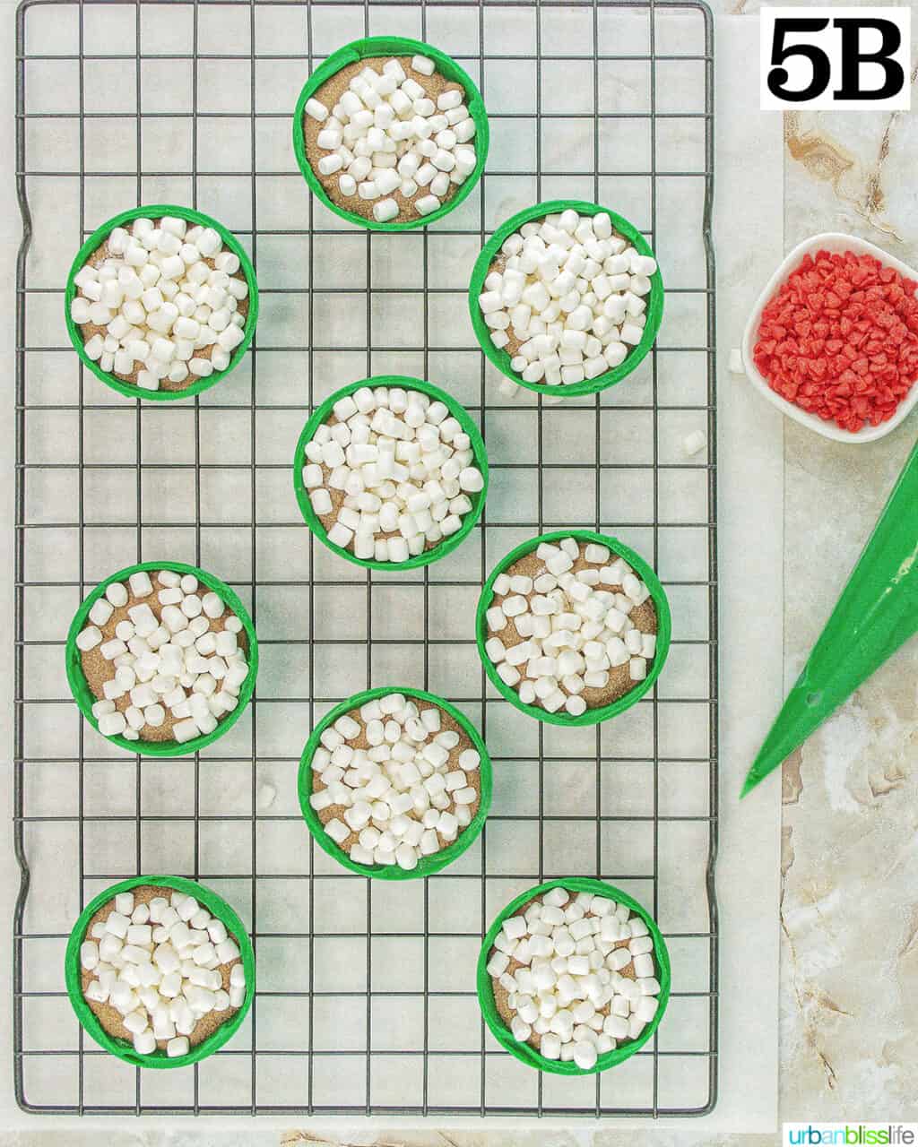 green halves of Grinch hot cocoa bombs with frosting, marshmallows, hot cocoa mix, and red heart sprinkles.