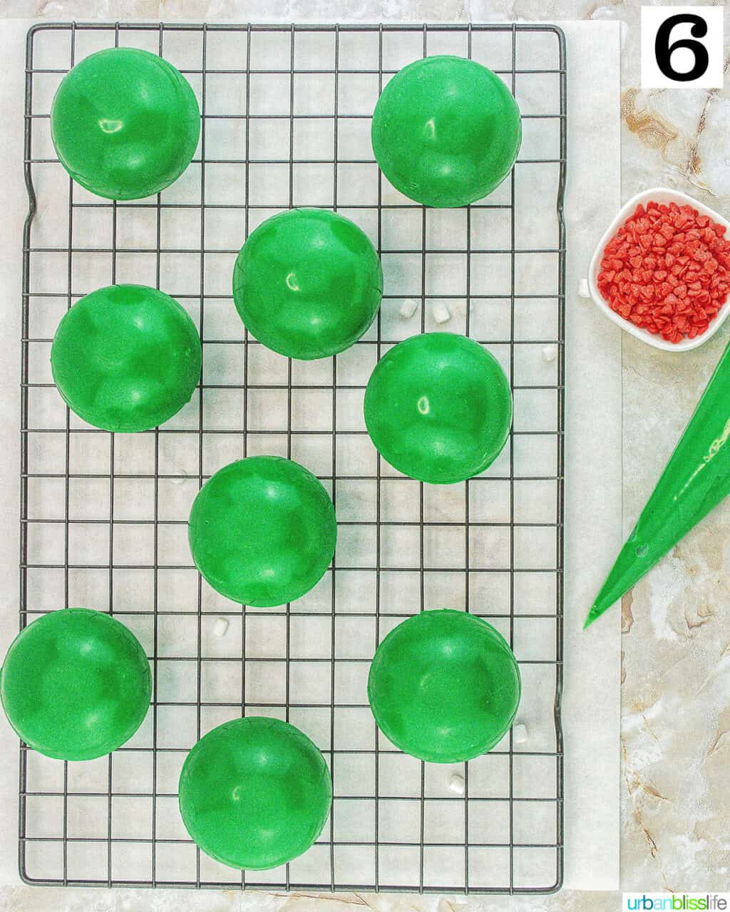 green halves of Grinch hot cocoa bombs with frosting, marshmallows, hot cocoa mix, and red heart sprinkles.