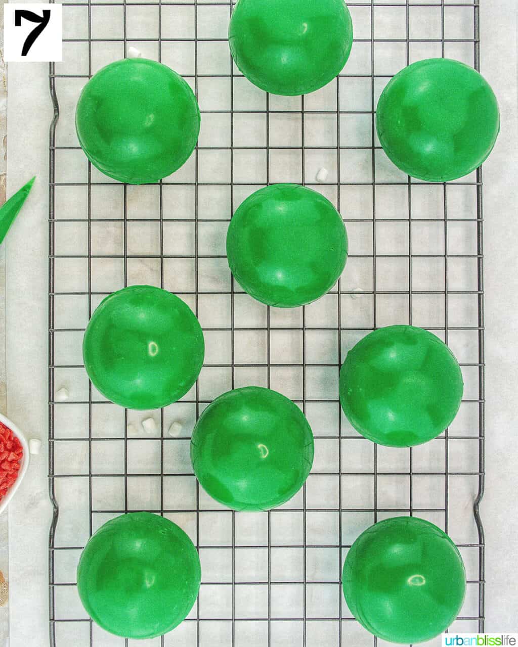 green halves of Grinch hot cocoa bombs with frosting, marshmallows, hot cocoa mix, and red heart sprinkles.