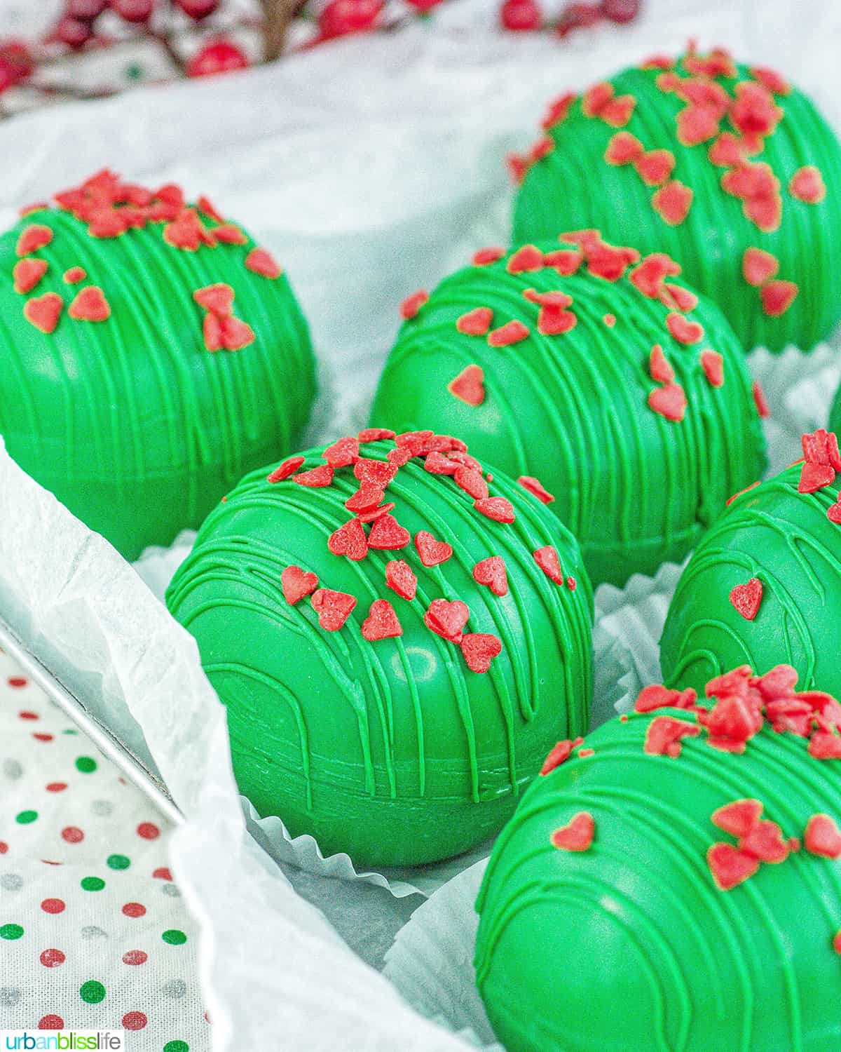 several bright green Grinch hot chocolate bombs with red heart sprinkles.