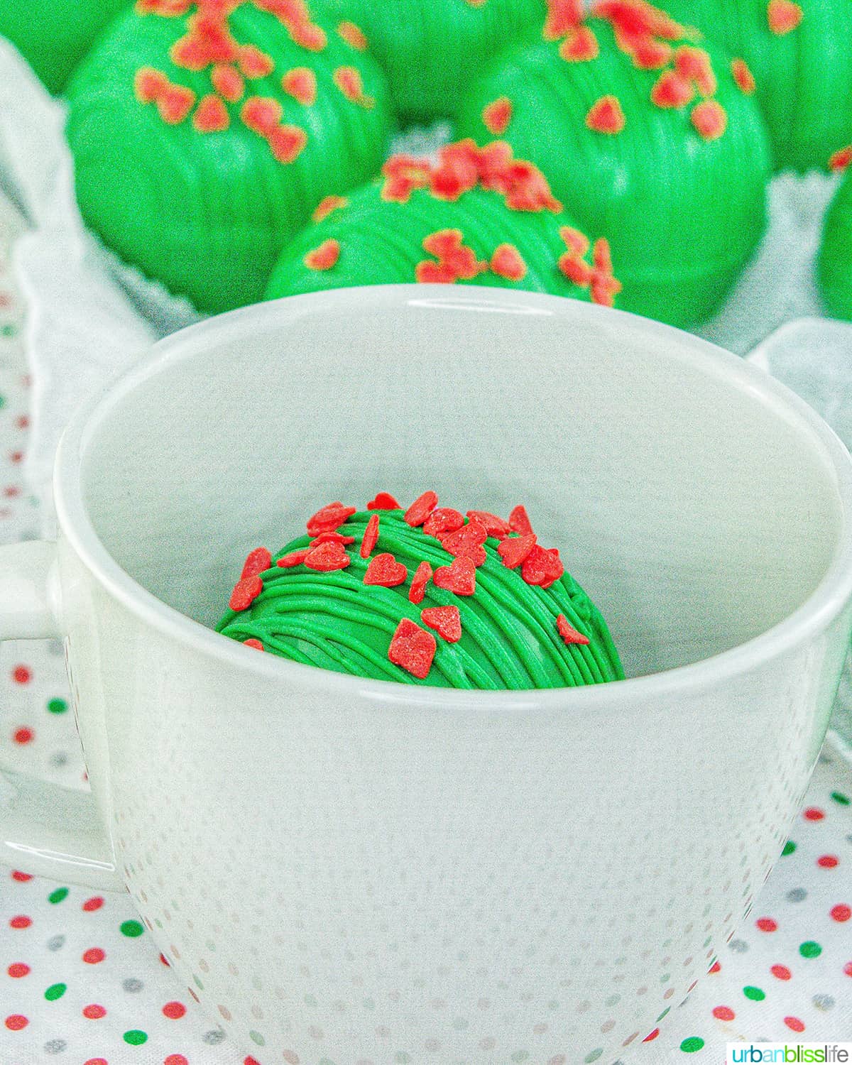 Grinch hot chocolate bombs around a mug of hot cocoa.