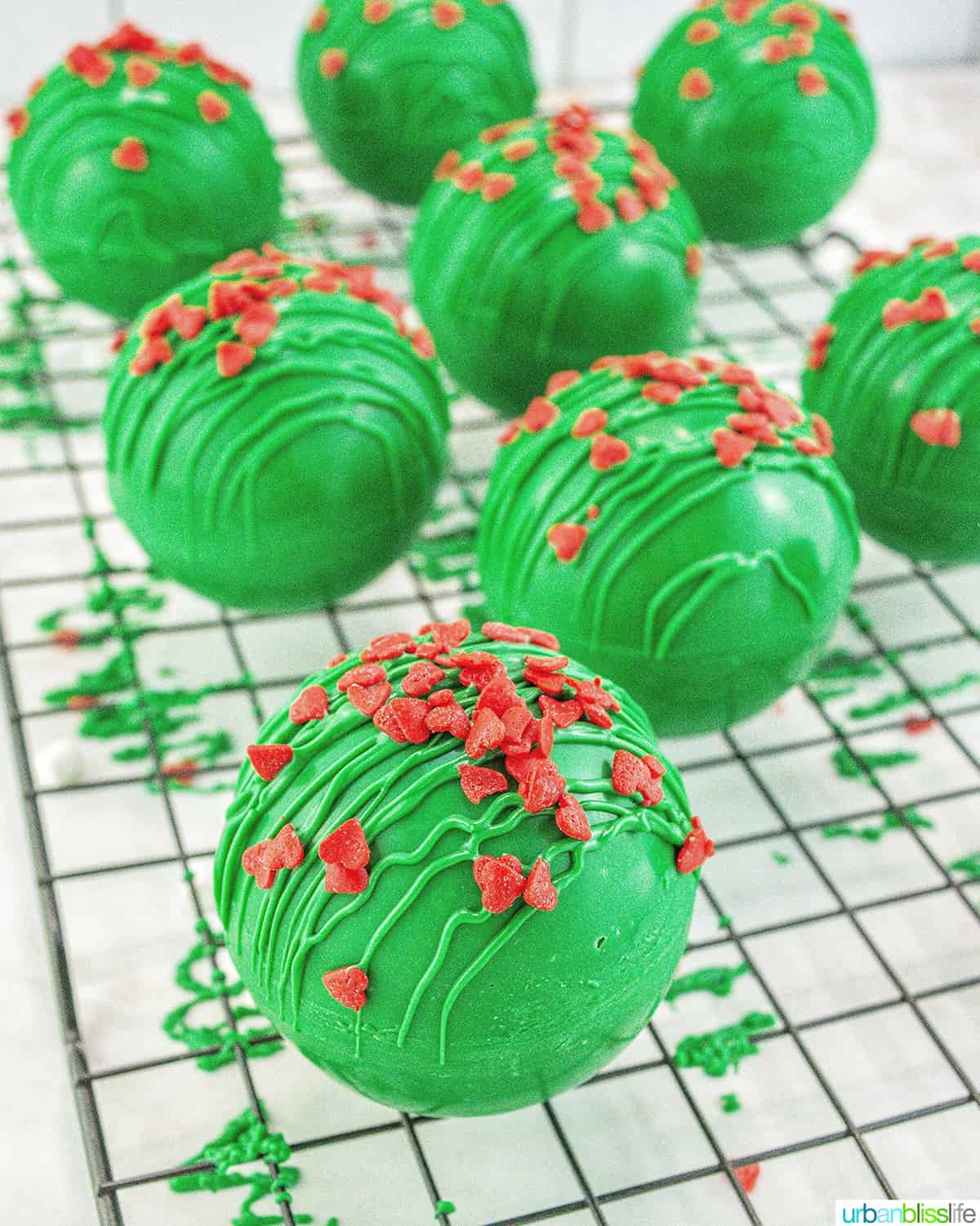 several bright green Grinch hot chocolate bombs with red heart sprinkles.