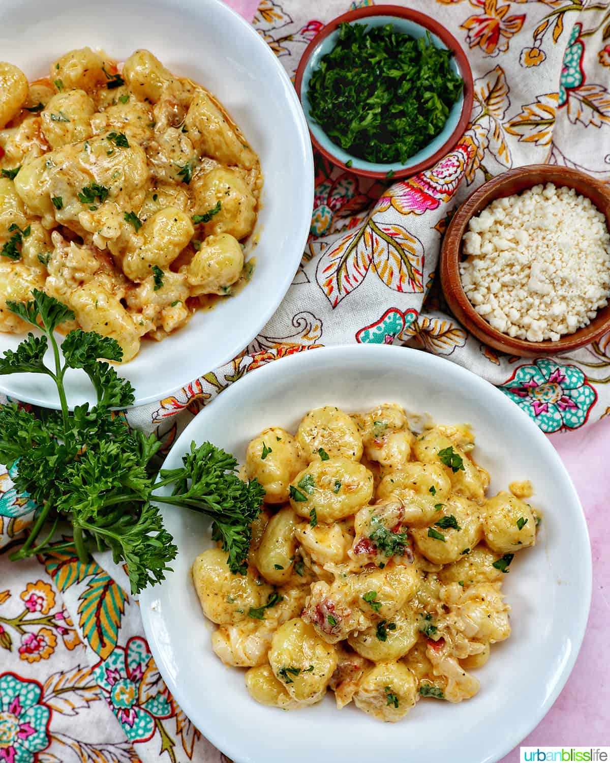 two bowls of lobster gnocchi with herbs and sides of garnishes.