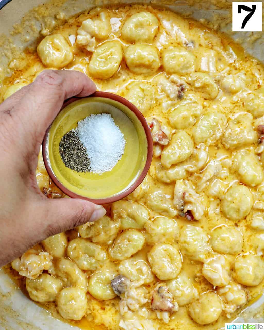 hand holding a bowl of salt and pepper over a skillet of lobster gnocchi.