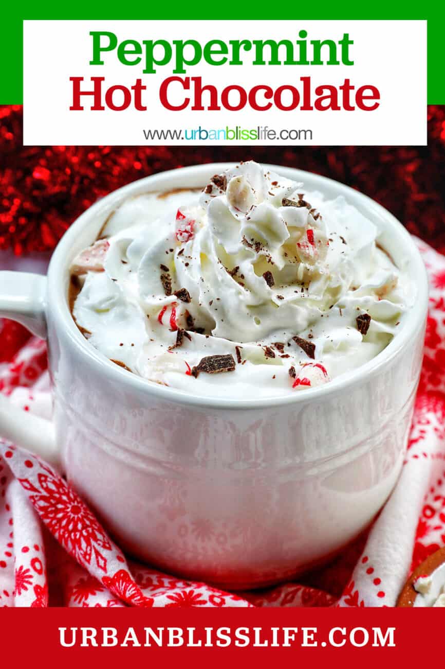 white mug with peppermint hot chocolate, whipped cream, surrounded by red and white Christmas decorations with title text that reads "Peppermint Hot Chocolate."