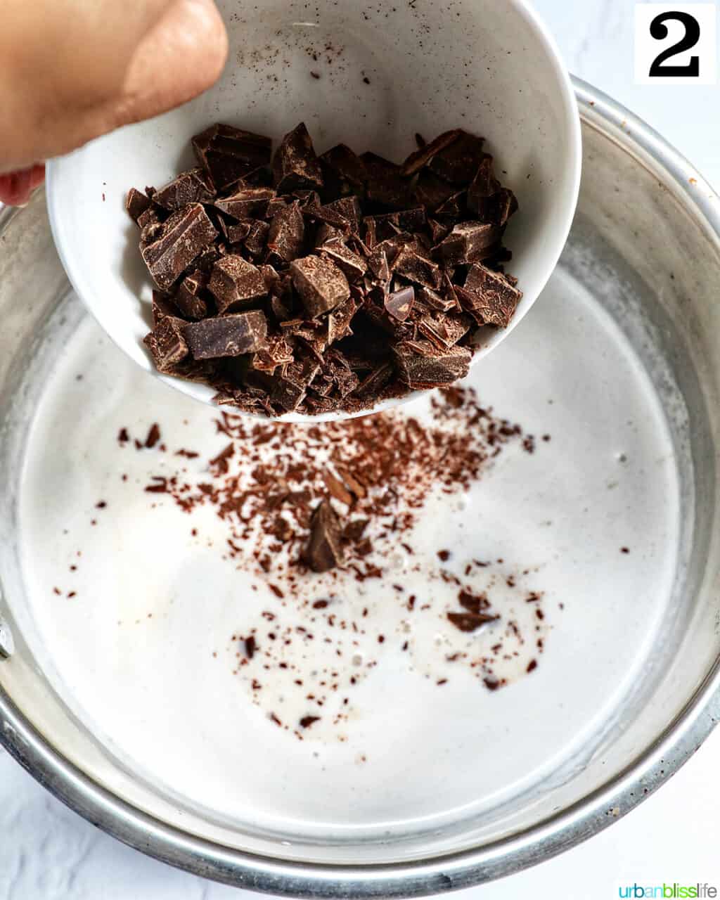 hand pouring shaved chocolate into a saucepan with cream.