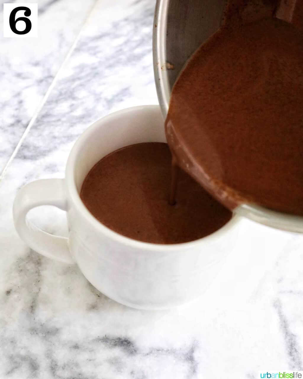 pouring peppermint hot chocolate from a saucepan into a large white mug.