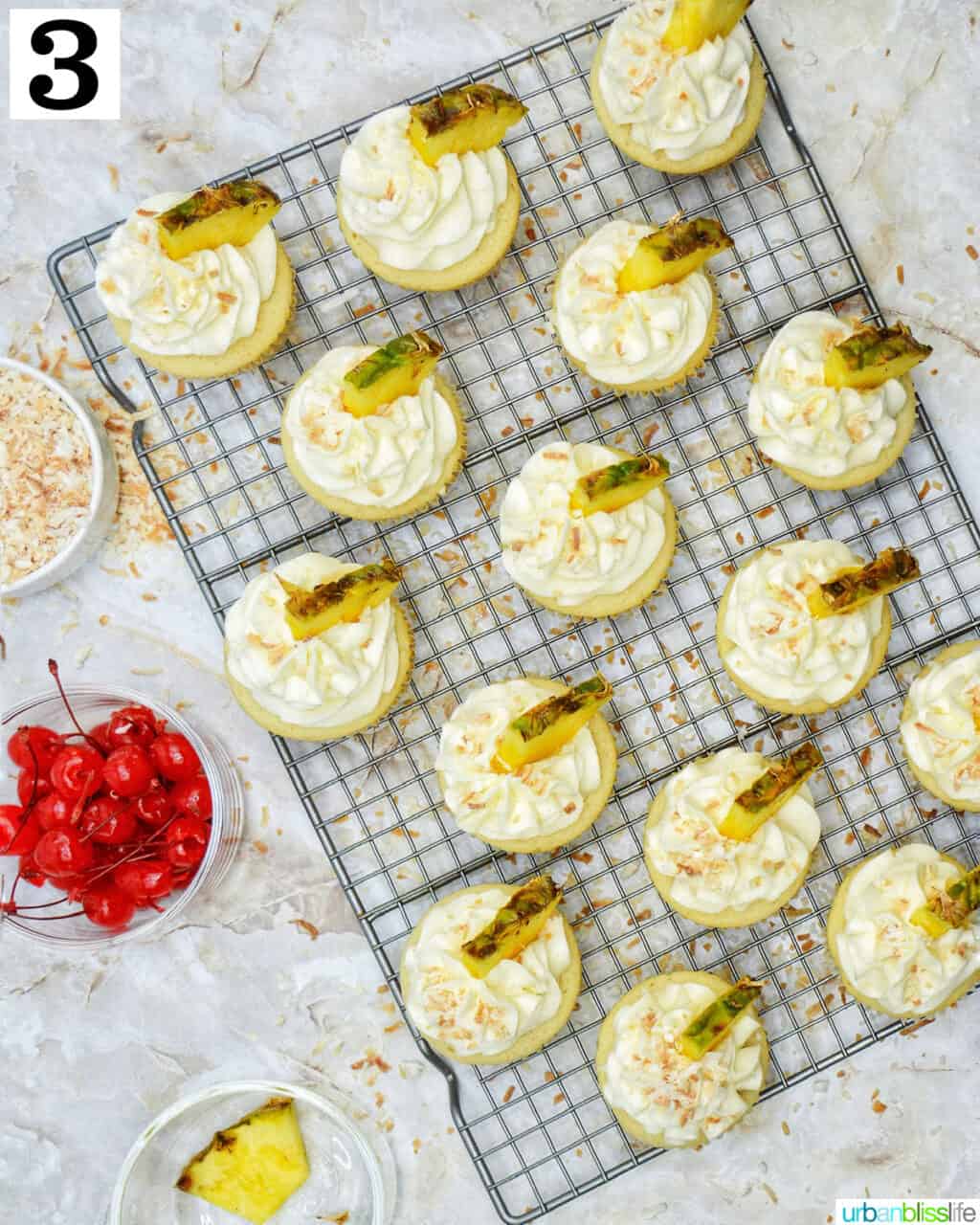 pina colada cupcakes frosted with lime slices on a wire rack.