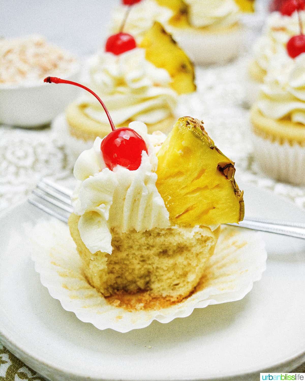 pina colada cupcakes with slice of pineapple, cut in half, on patterned table.