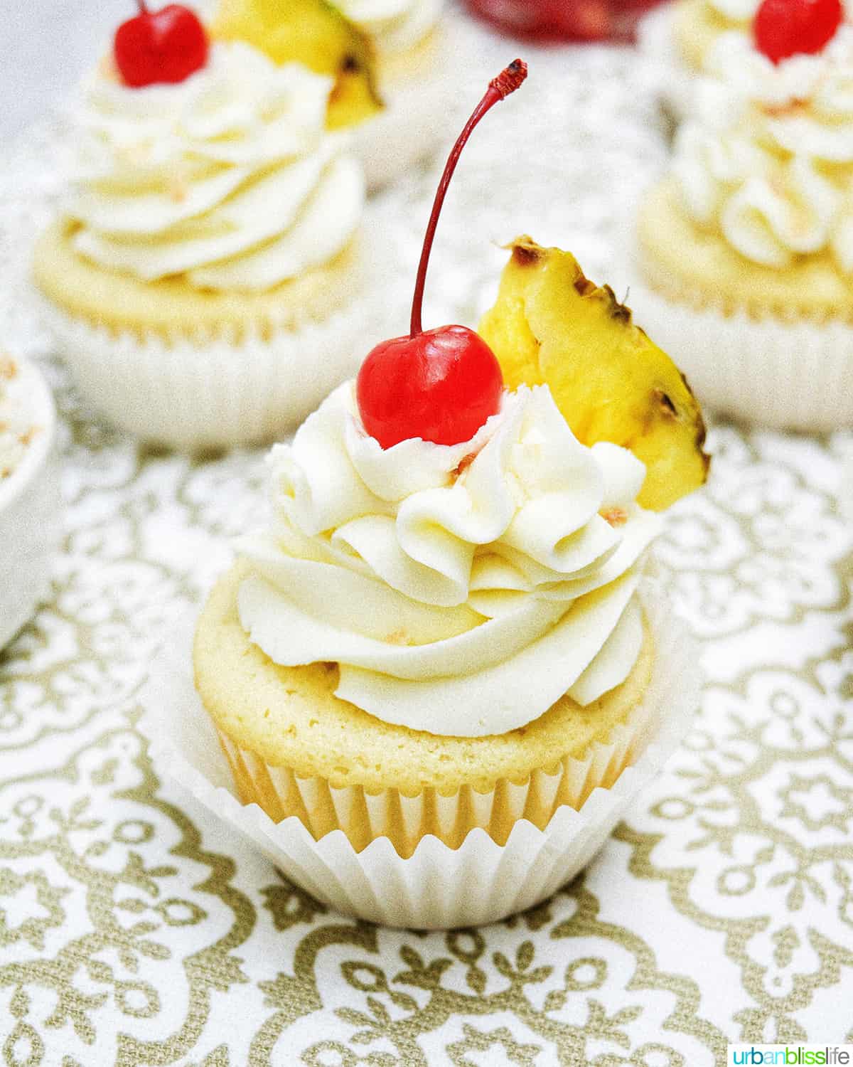 pina colada cupcakes with slice of pineapple on patterned table.