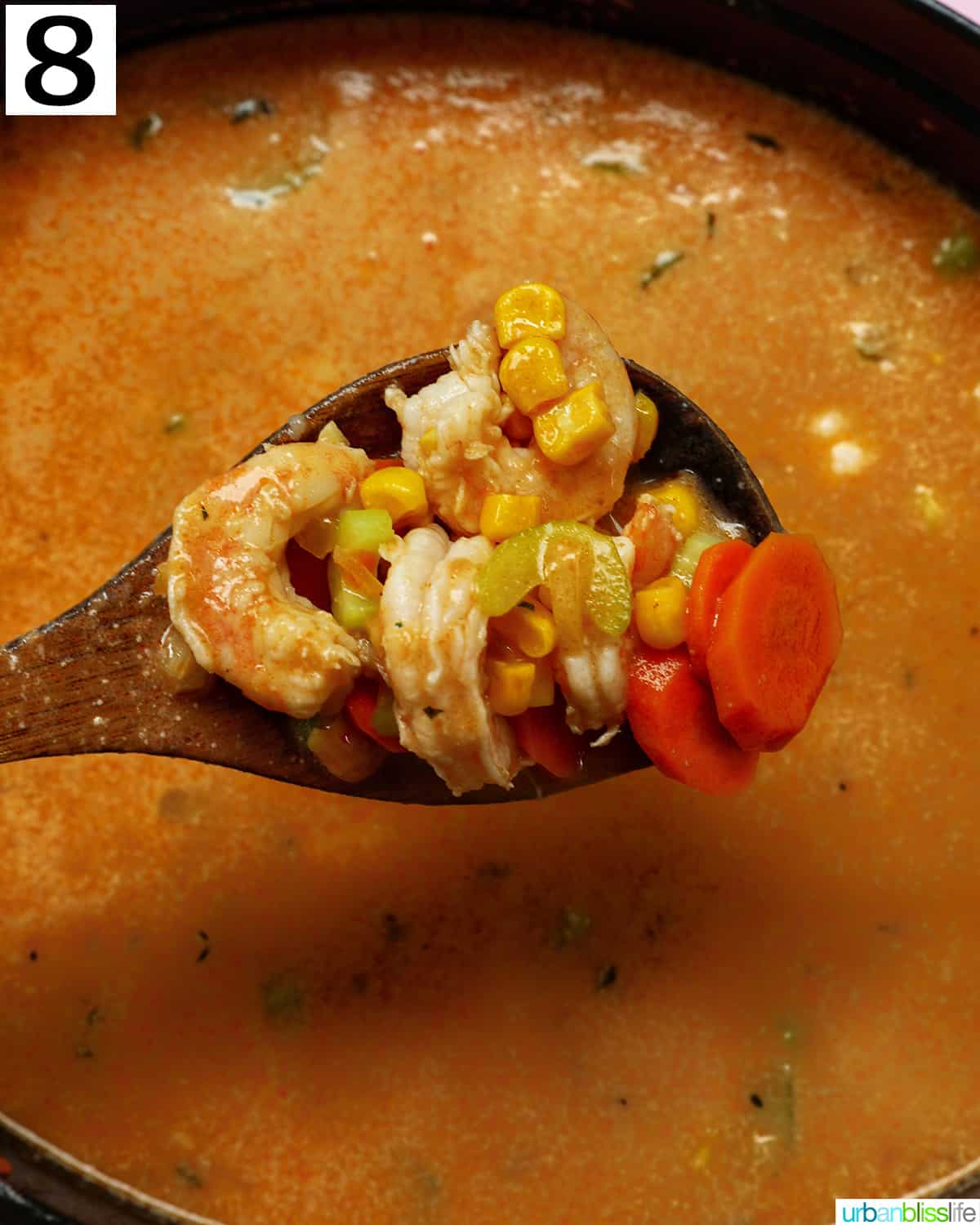 wooden spoon holding shrimp and vegetables above a dutch oven full of soup.