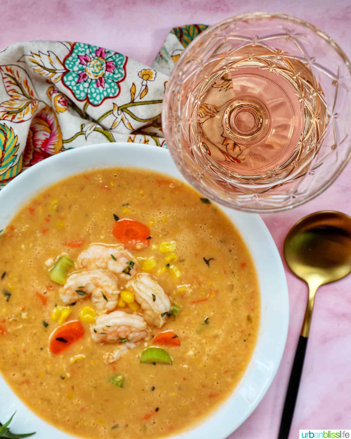 glass of rosé wine above a bowl of shrimp and corn bisque.