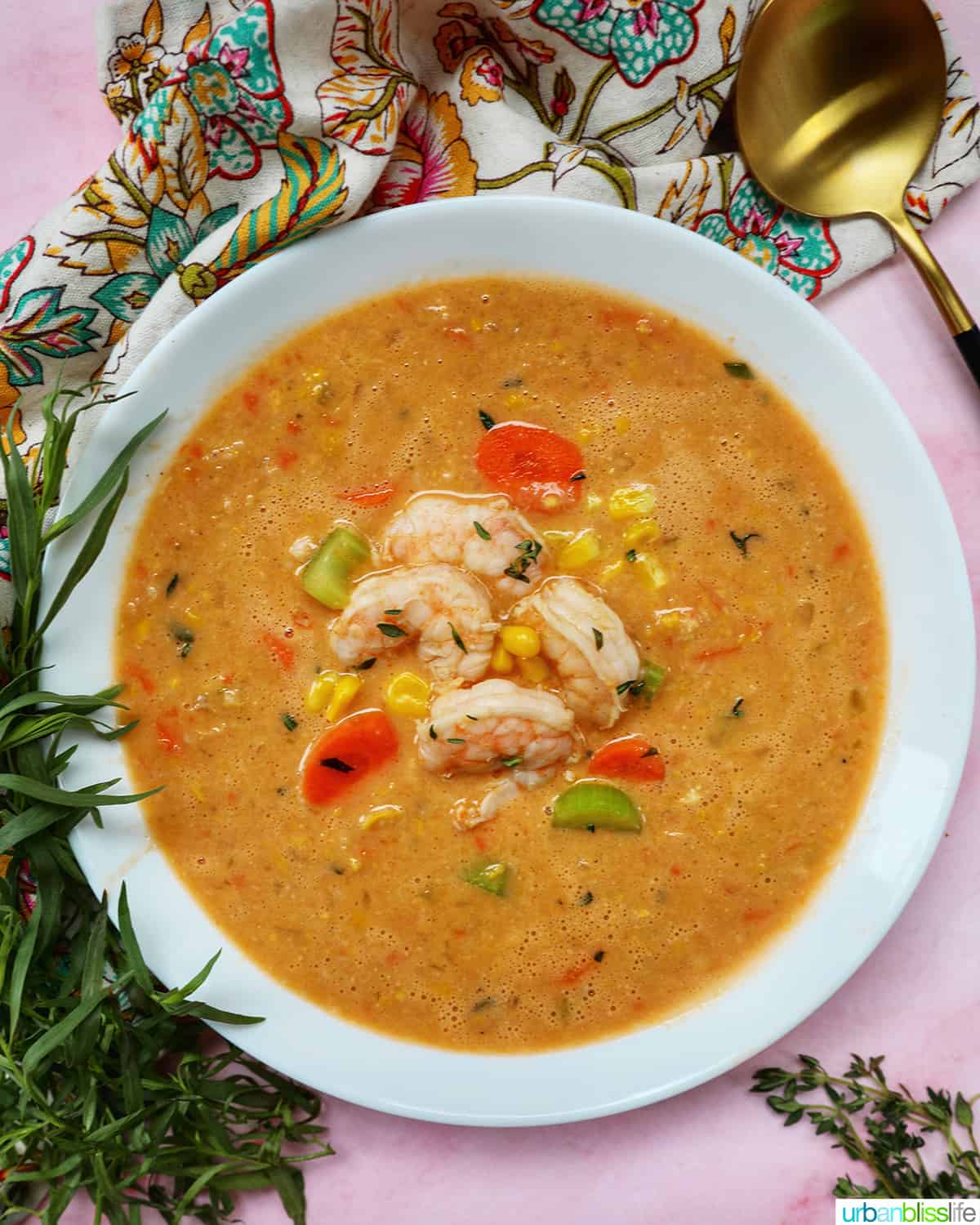 bowl of shrimp corn bisque with fresh herbs and gold spoon.
