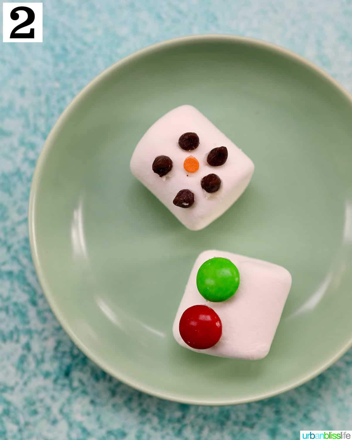 marshmallows with chocolate chips for eyes and mouth on a green plate.