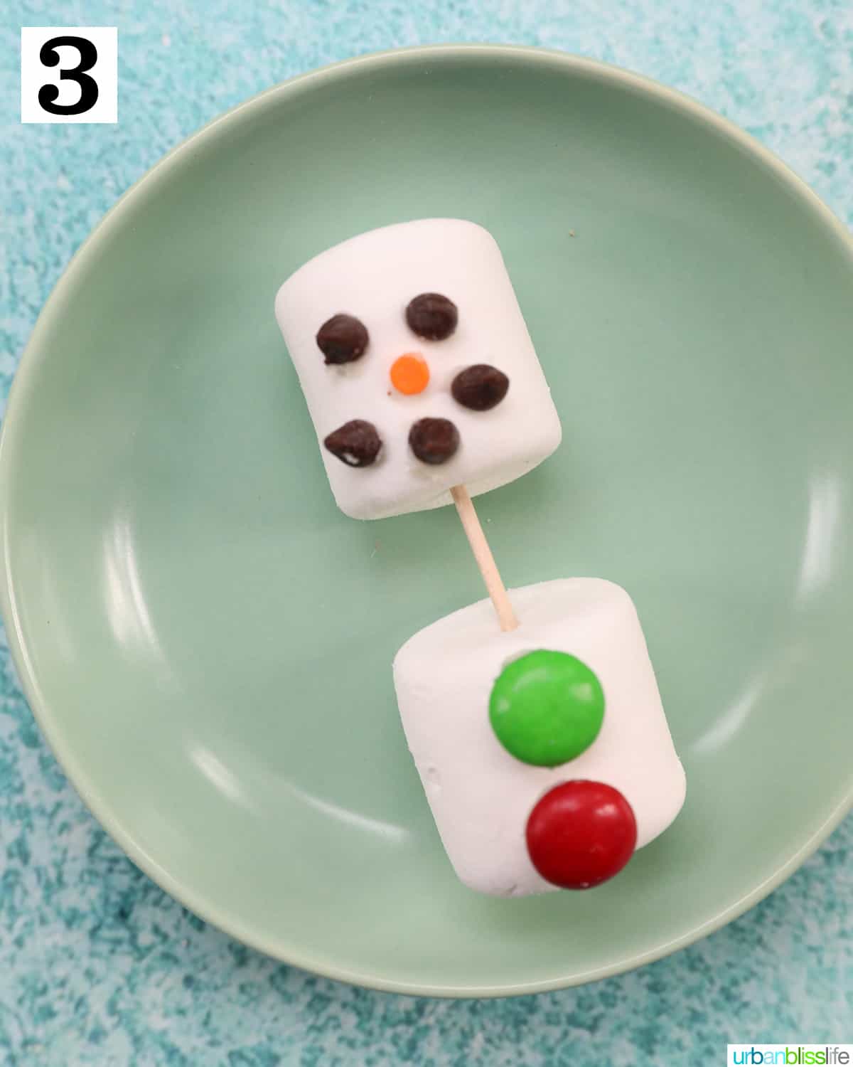 marshmallows with chocolate chips for eyes and mouth on a green plate.