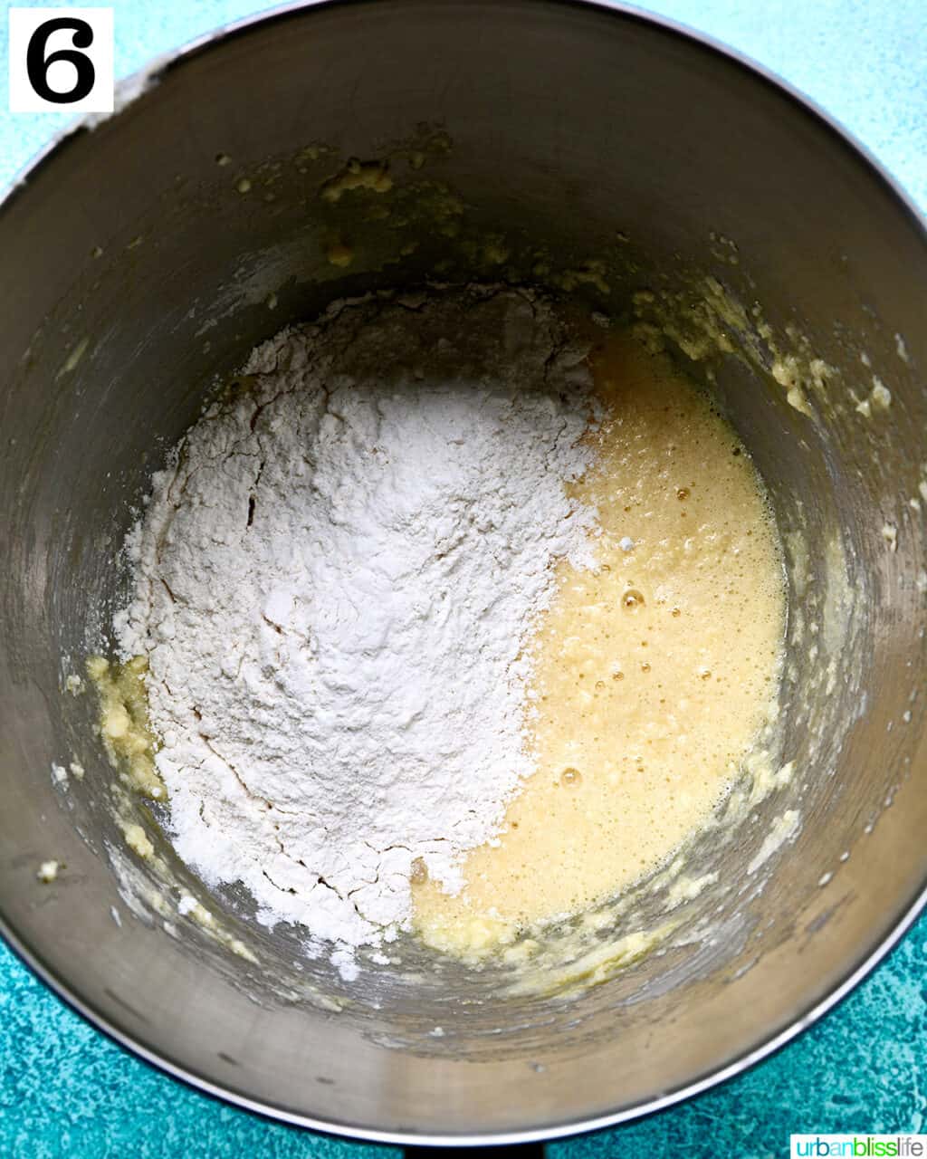adding dry ingredients to wet ingredients in a stainless steel bowl.