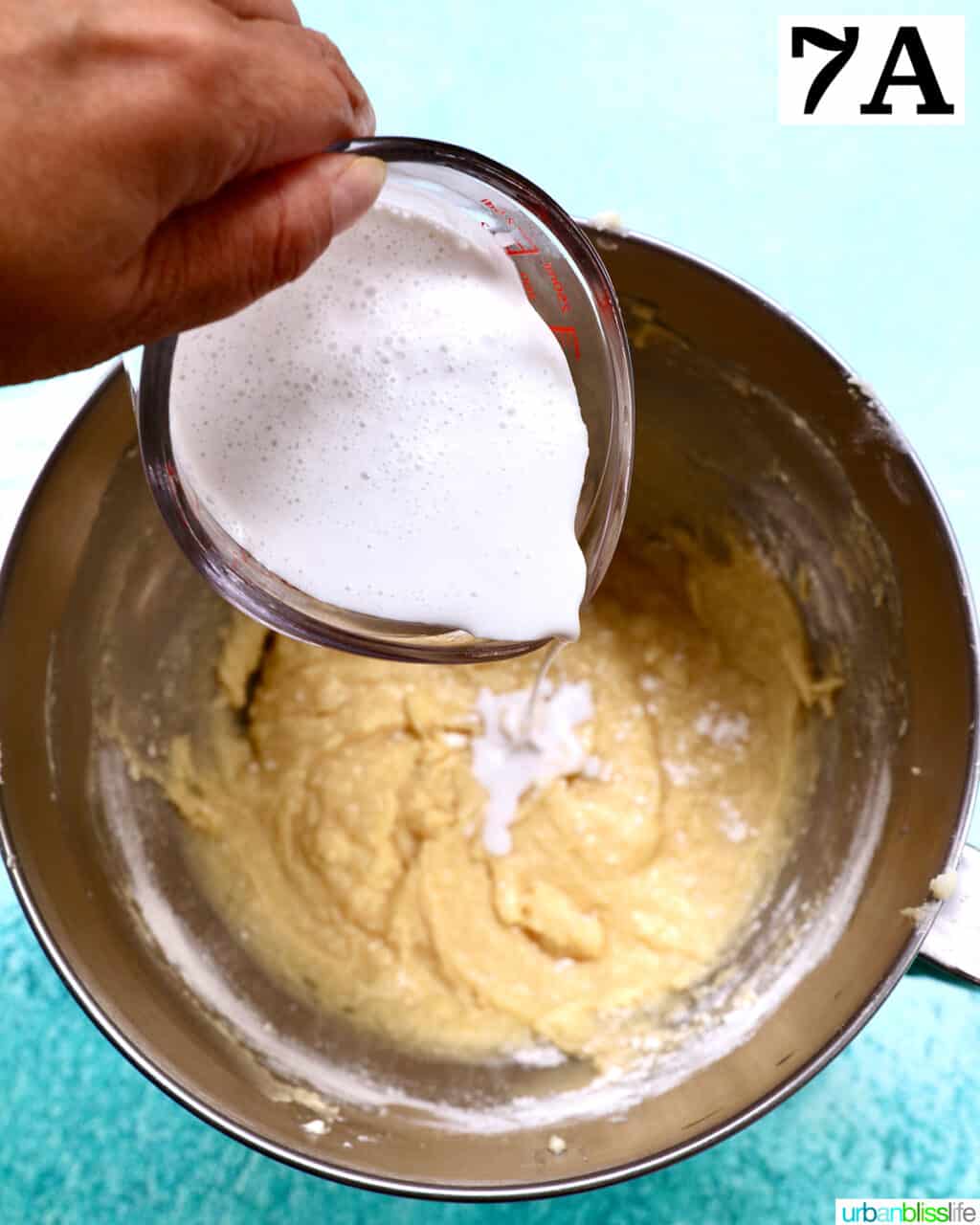 adding milk to cupcake batter in a stainless steel bowl.