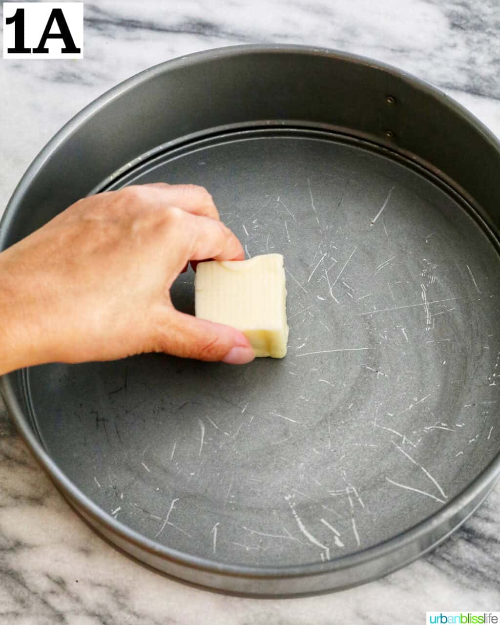 hand greasing a springform pan with butter.