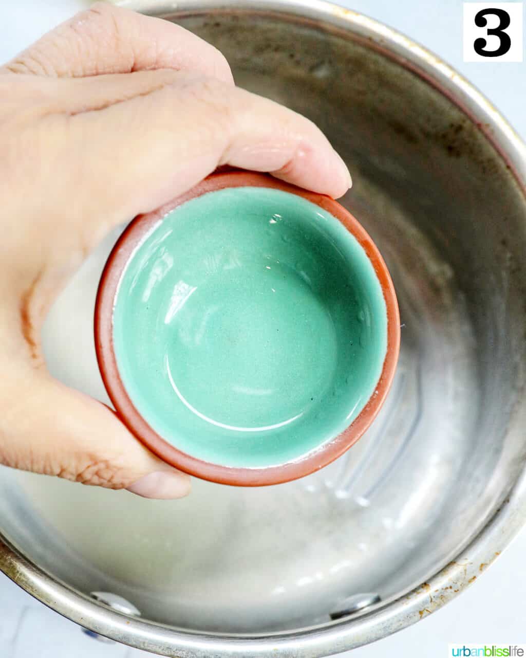 hand holding a small bowl of peppermint extract over a saucepan.