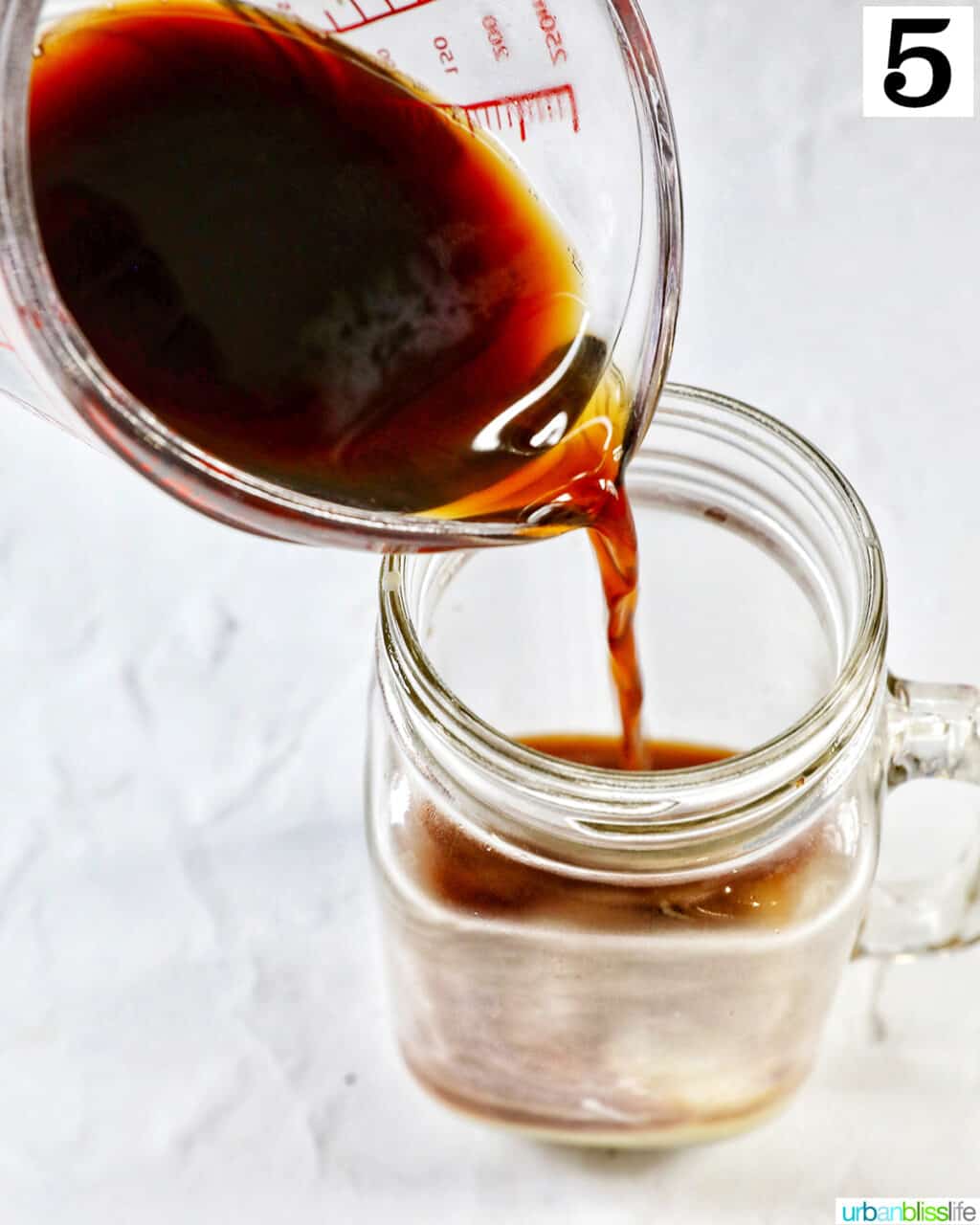 pouring brewed coffee into a clear glass mug.