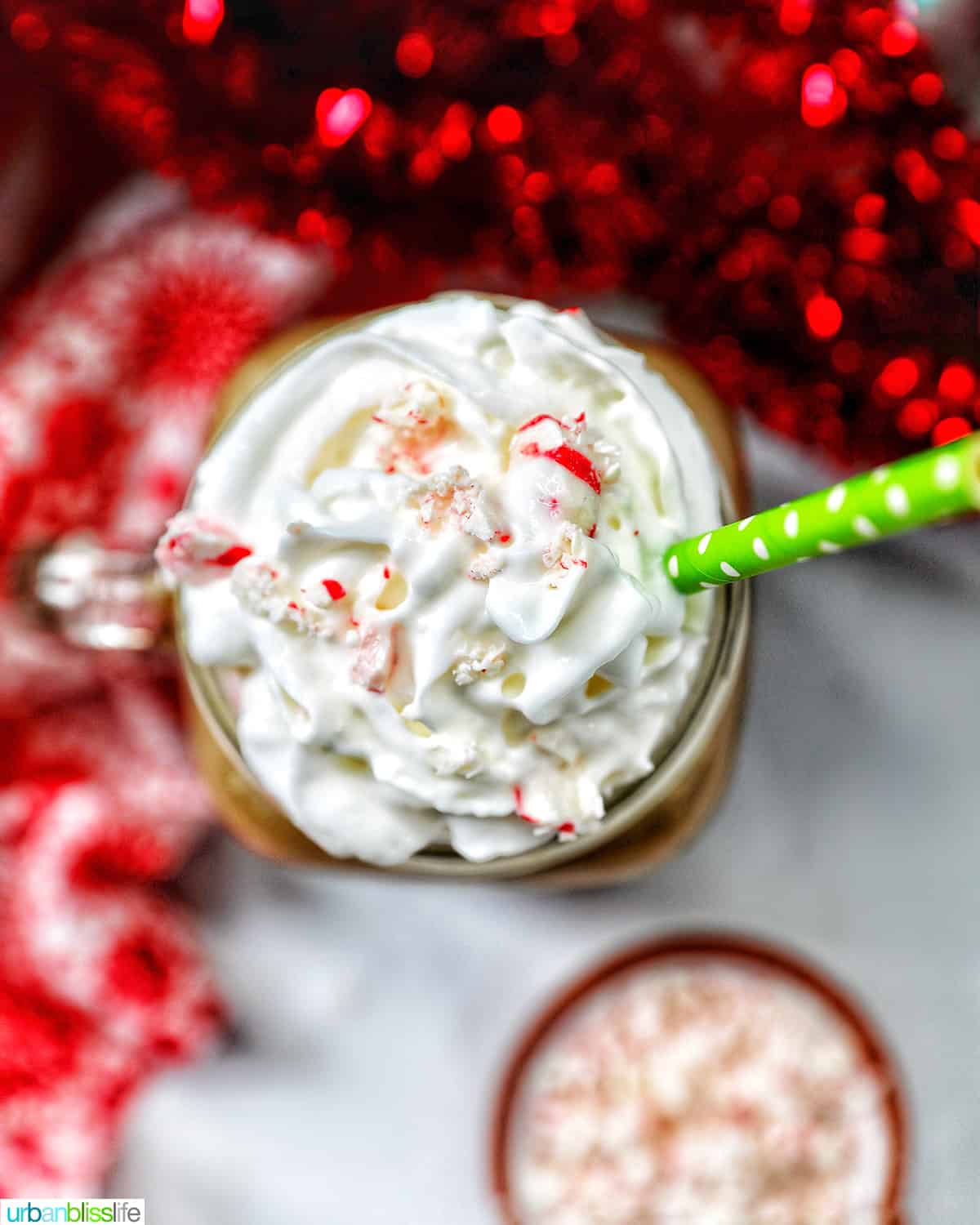 glass mug of white chocolate peppermint mocha with whipped cream with Christmas holiday decorations in the background.
