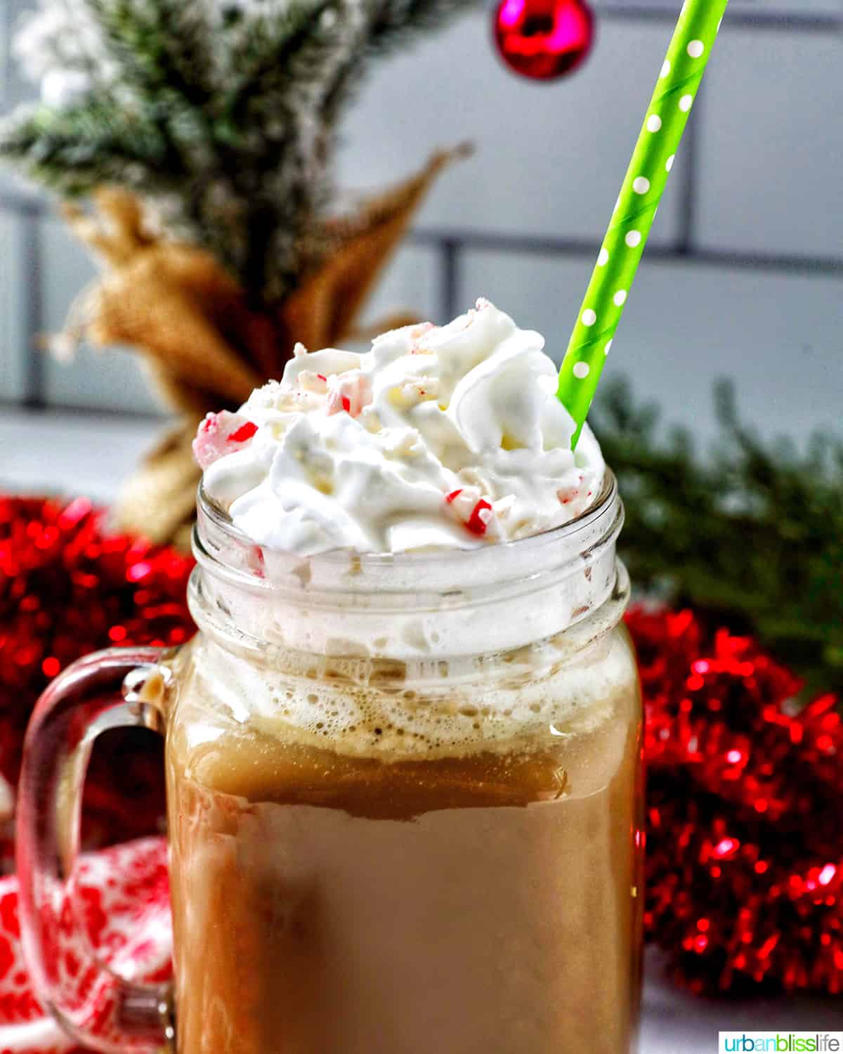 glass mug of white chocolate peppermint mocha with whipped cream and a green straw.