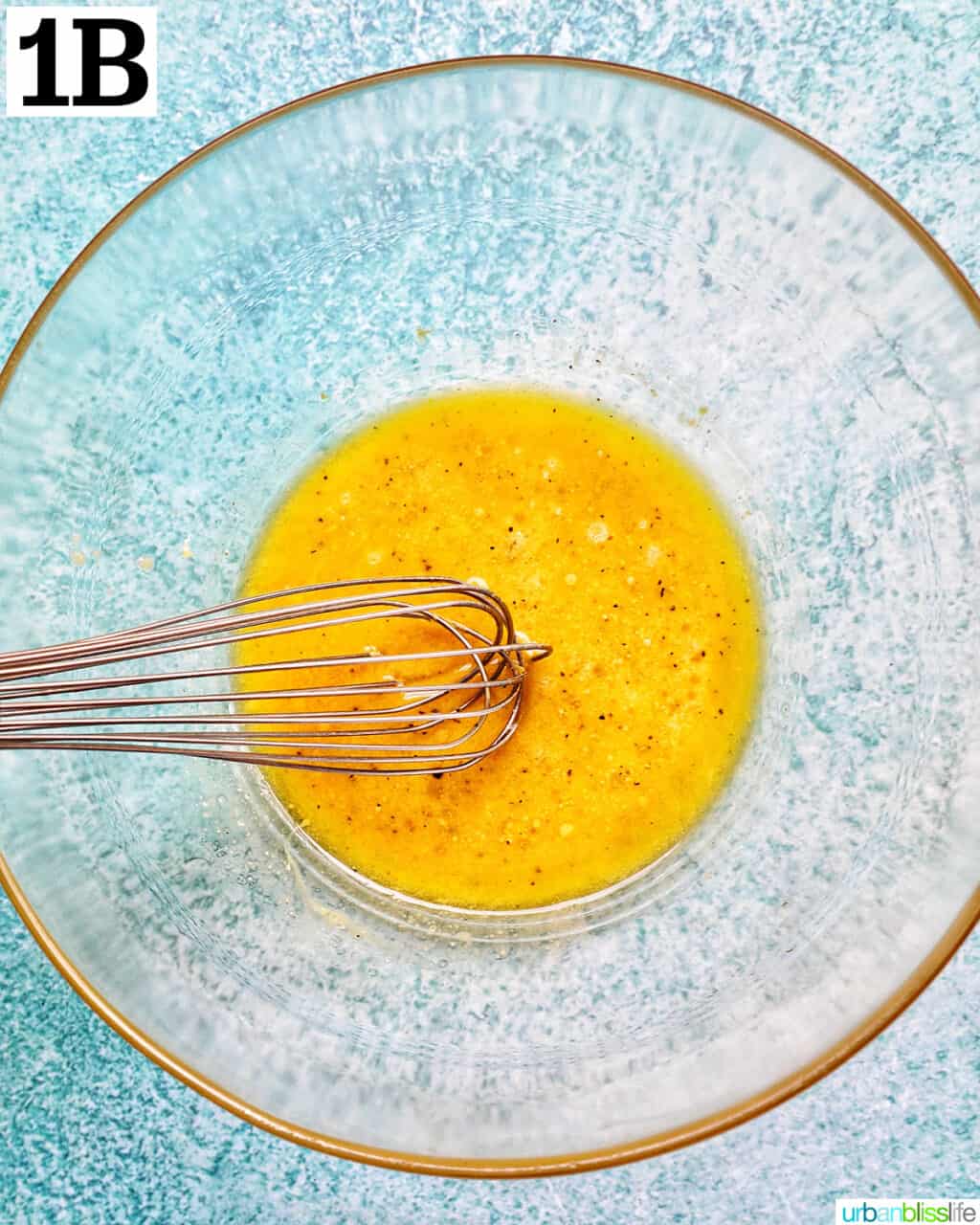 whisk and large glass bowl with salad dressing ingredients.