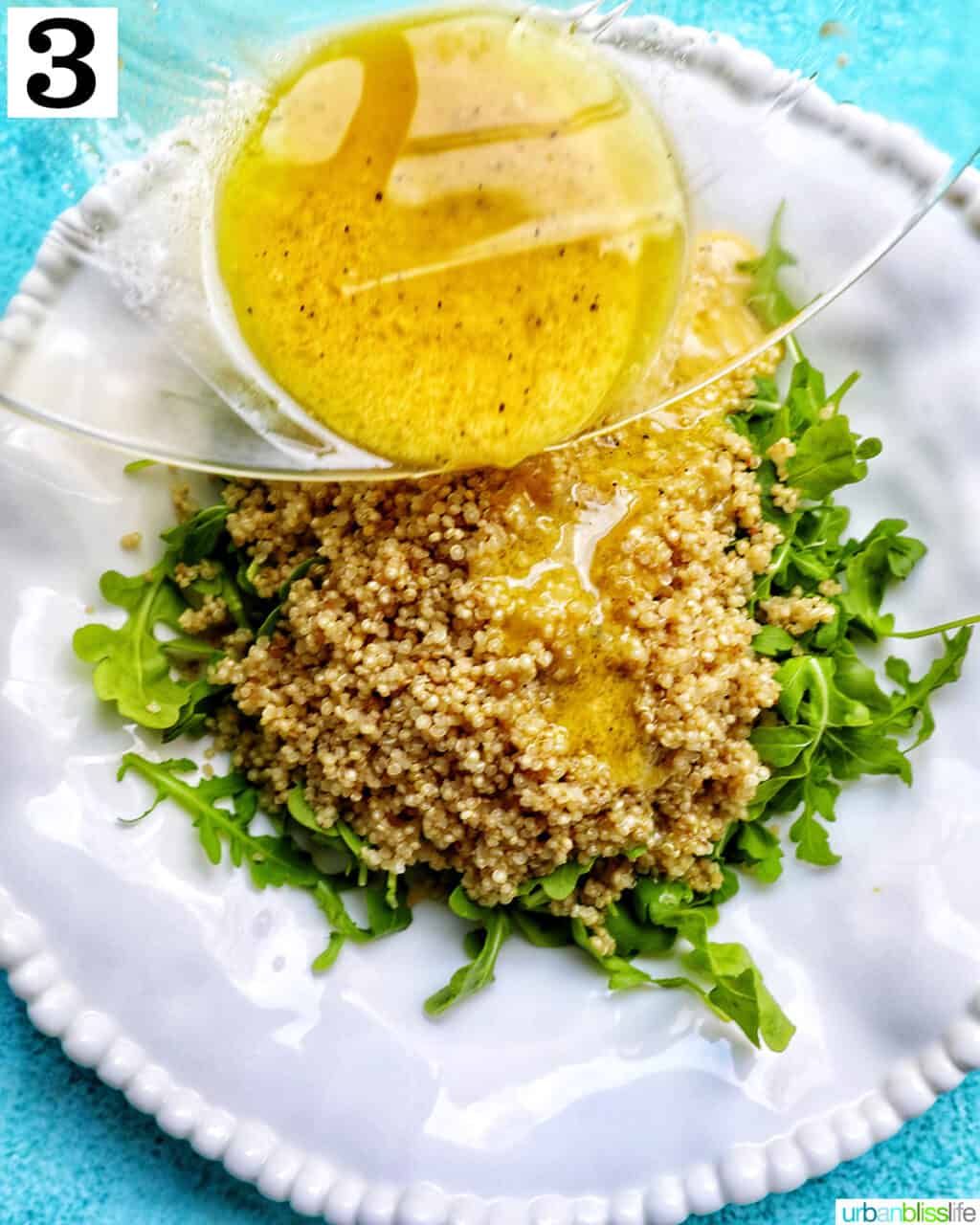 pouring salad dressing over a white bowl with arugula and quinoa salad.