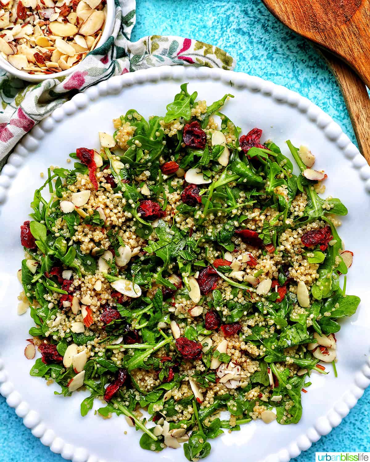 white bowl with arugula and quinoa salad with sliced almonds and dried cranberries.