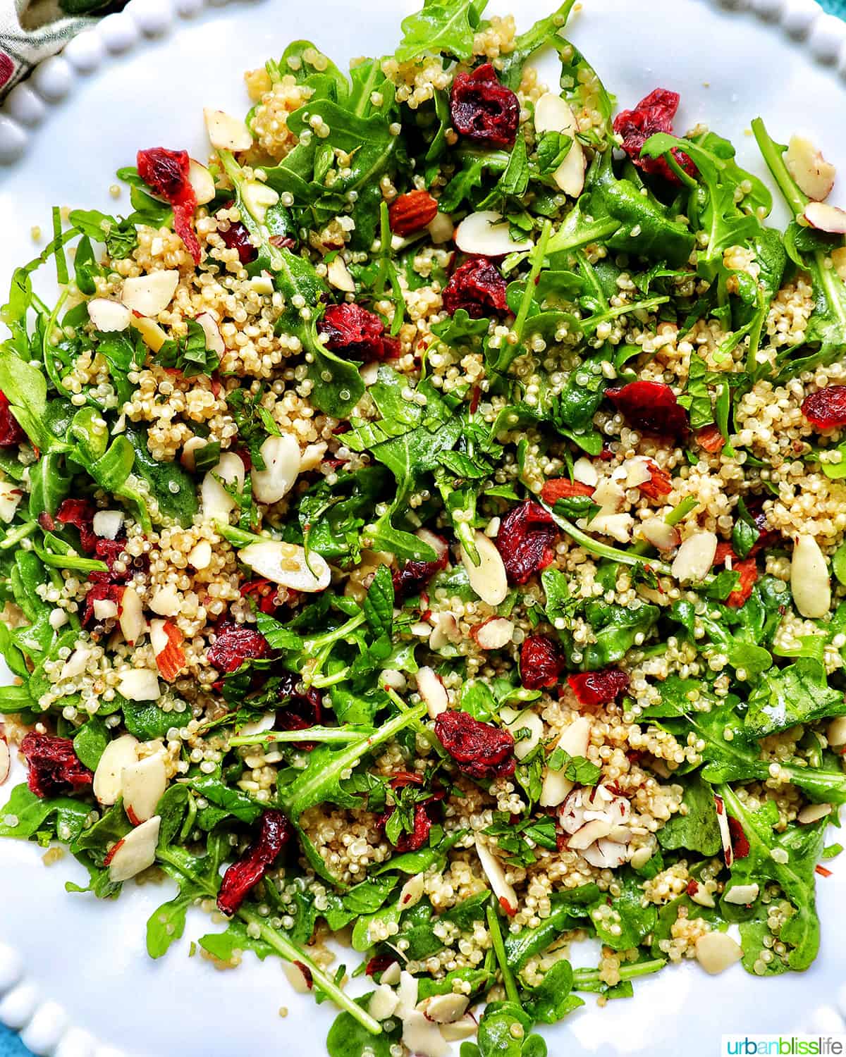 white bowl with arugula and quinoa salad with sliced almonds and dried cranberries.