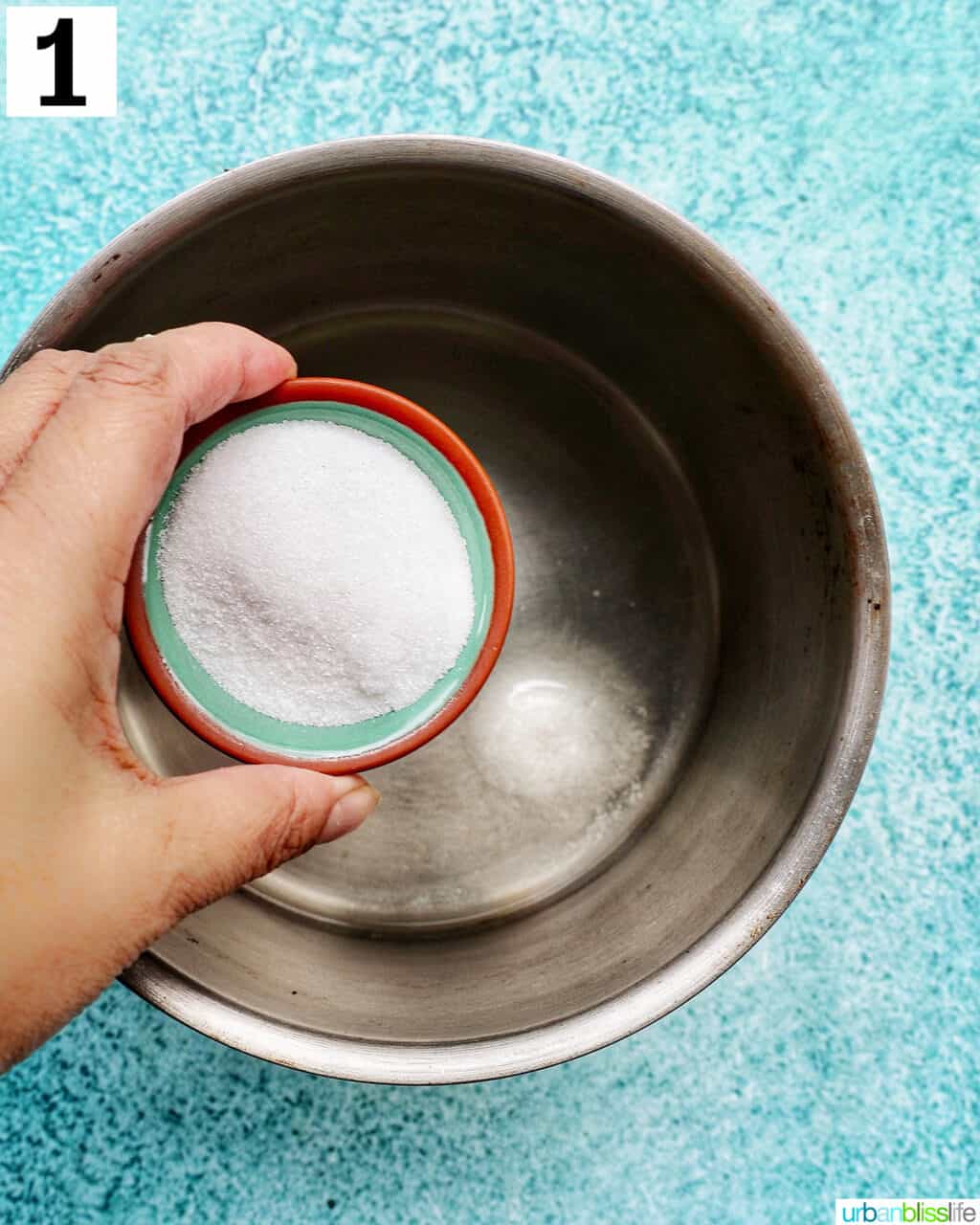 hand adding sugar to water in a small pot.