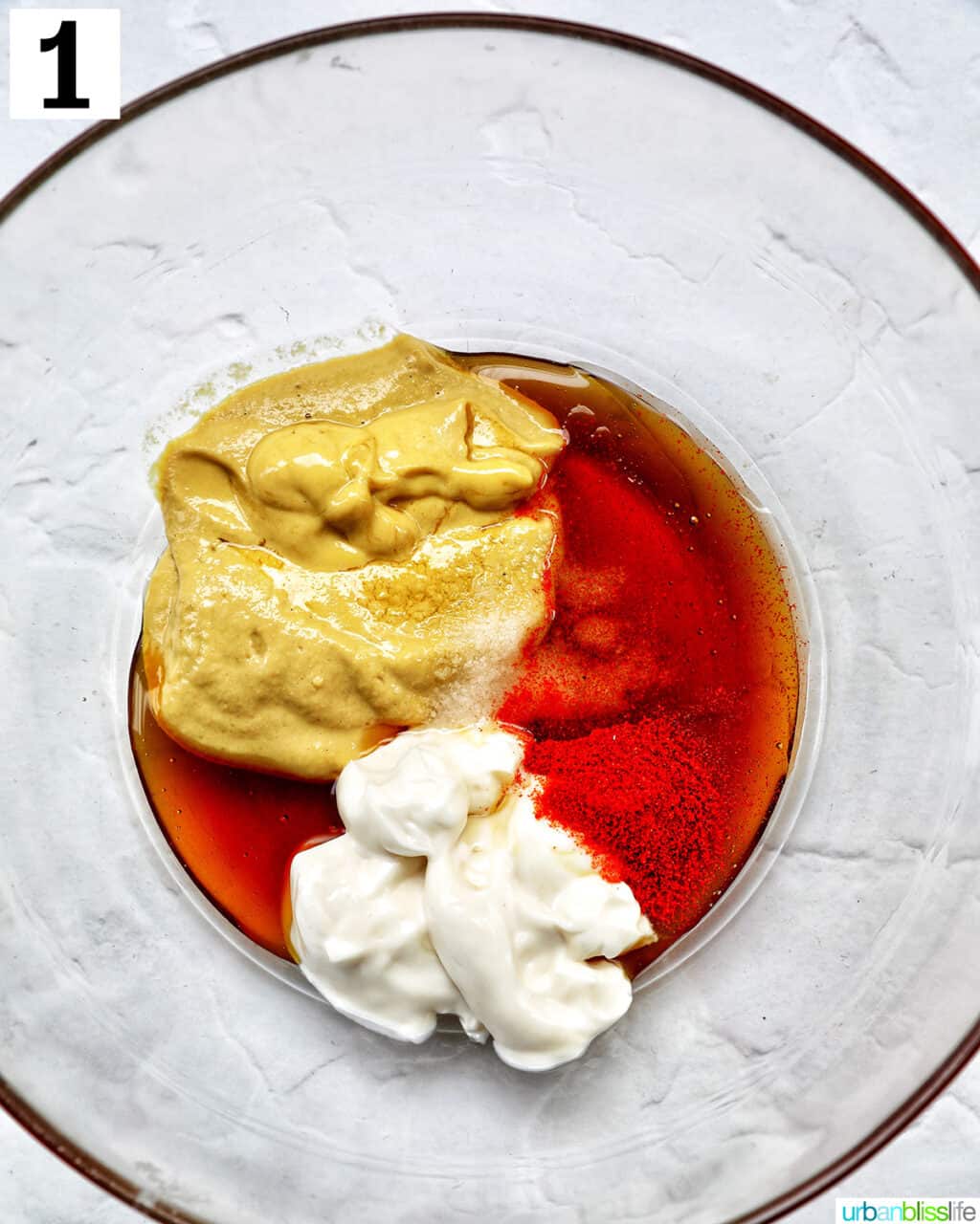 clear glass bowl with ingredients to make hand dipping a chicken tender into a bowl of honey mustard dipping sauce.