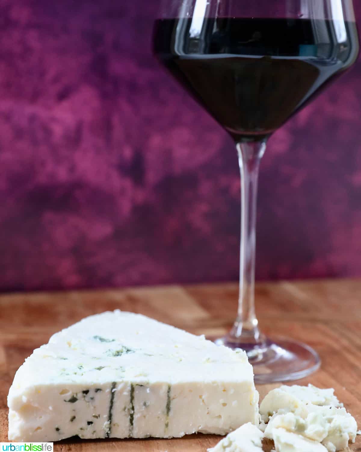 glass of Malbec red wine with a wedge of blue cheese against a purple backdrop.