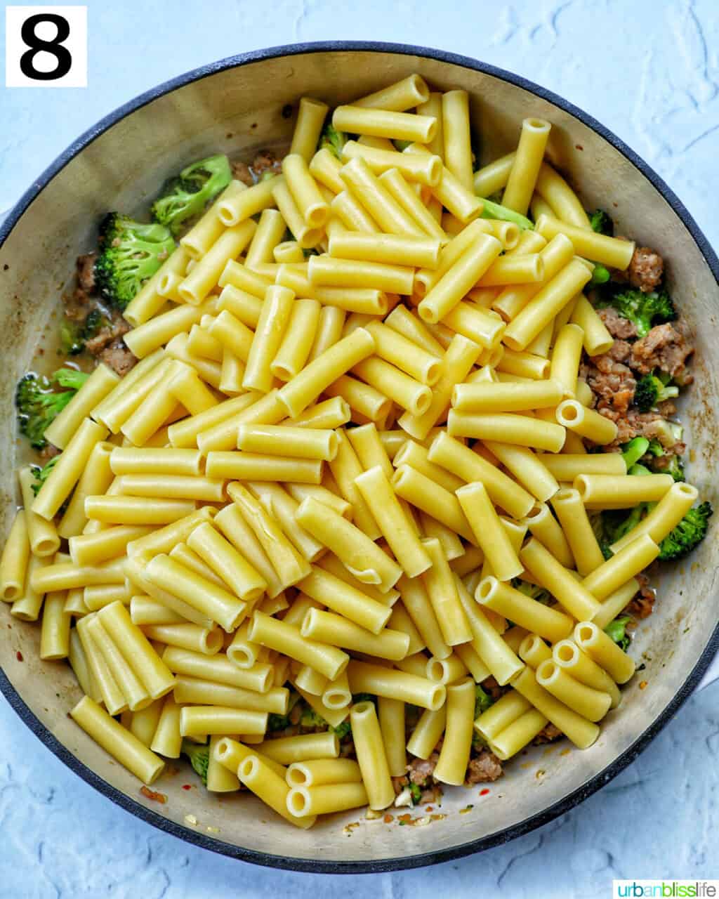 ziti pasta added to a large skillet of broccoli and Italian sausage.
