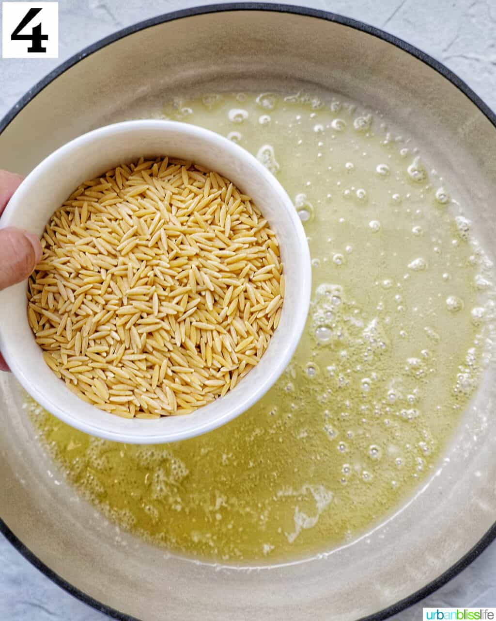 bowl of uncooked orzo over a skillet with melted butter.