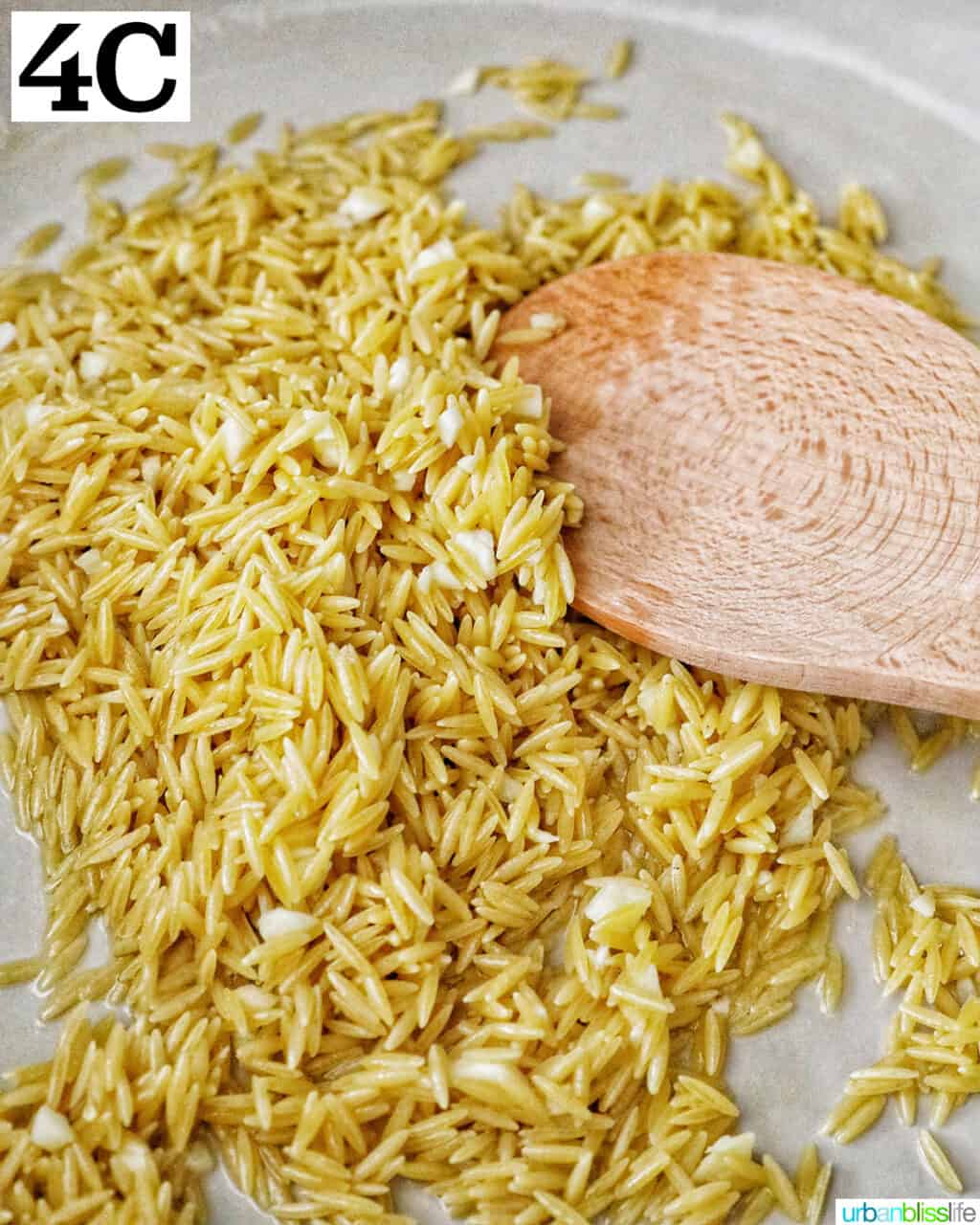 wooden spoon stirring orzo and garlic in a large skillet.
