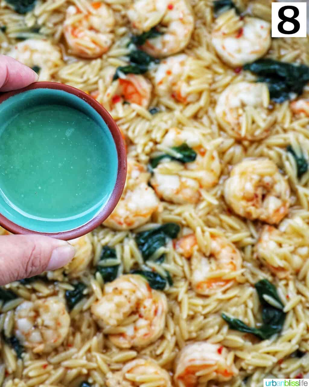 small bowl of lemon juice over a skillet of shrimp scampi and orzo.
