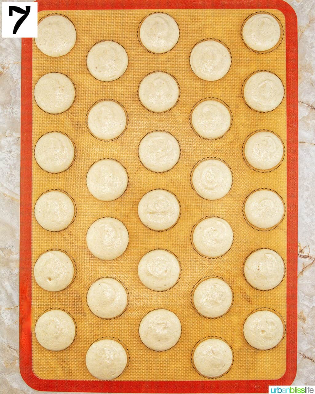 baking sheet with silicone mat and macaron cookie batter piped on it.