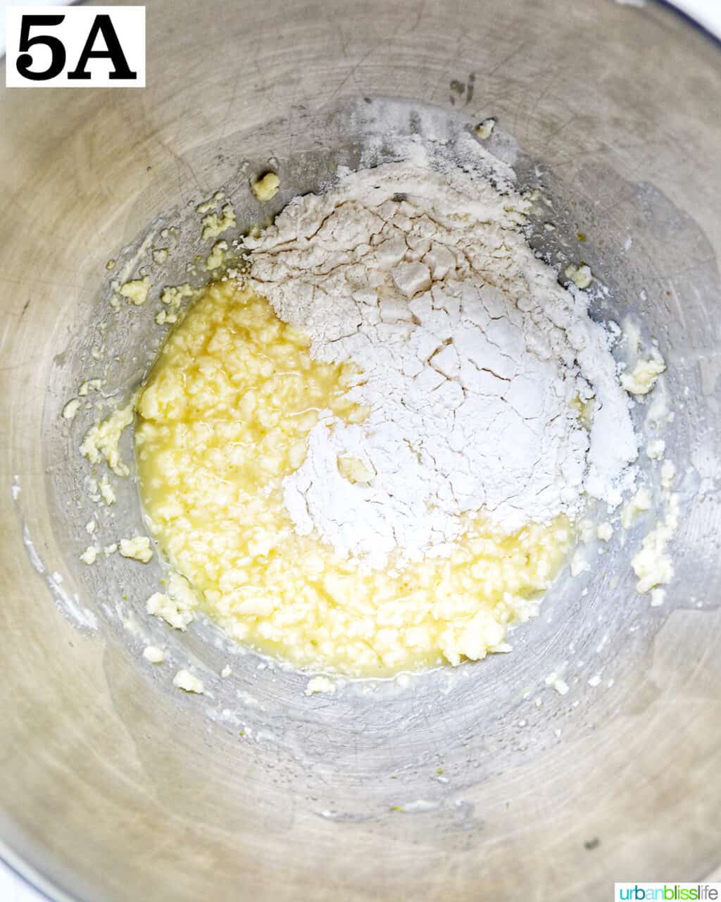 Adding dry ingredients to wet ingredients in the stainless steel bowl of a stand mixer.