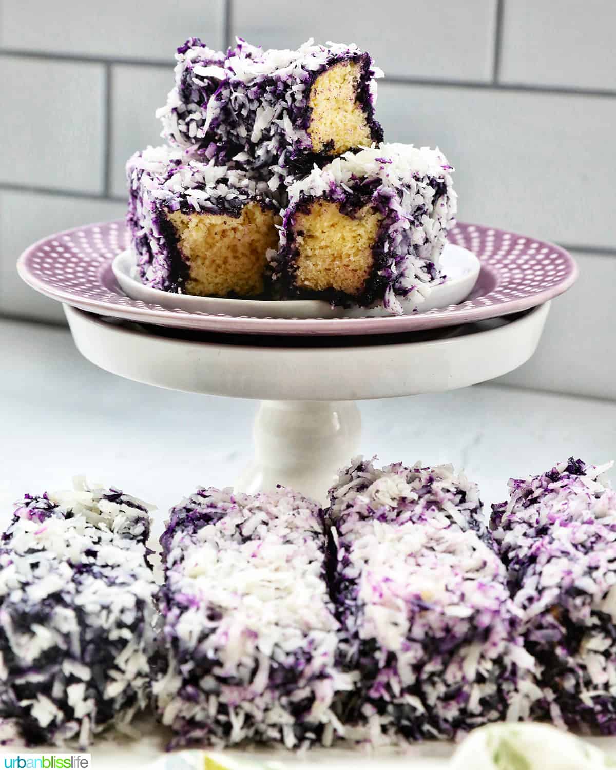 stack of ube bars sliced on a purple plated pedestal with a row of ube bars beneath.