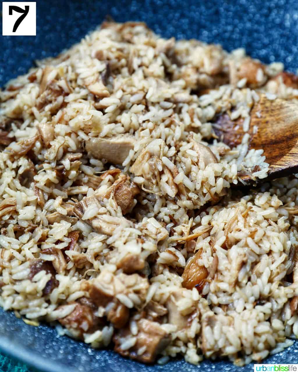 wooden spoon stirring adobo fried rice in a wok.