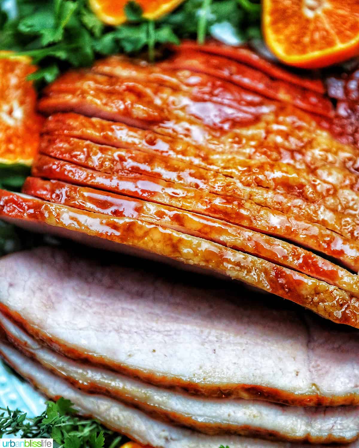 sliced honey glazed air fryer ham on a plate with fresh herbs and sliced oranges.