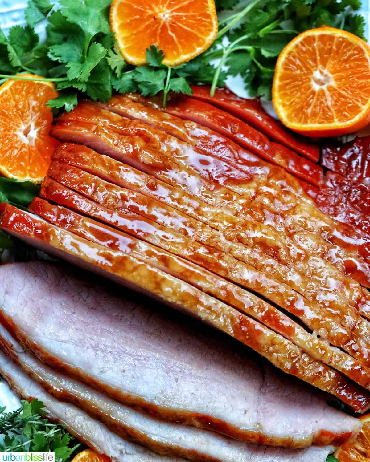 sliced honey glazed air fryer ham on a plate with fresh herbs and sliced oranges.