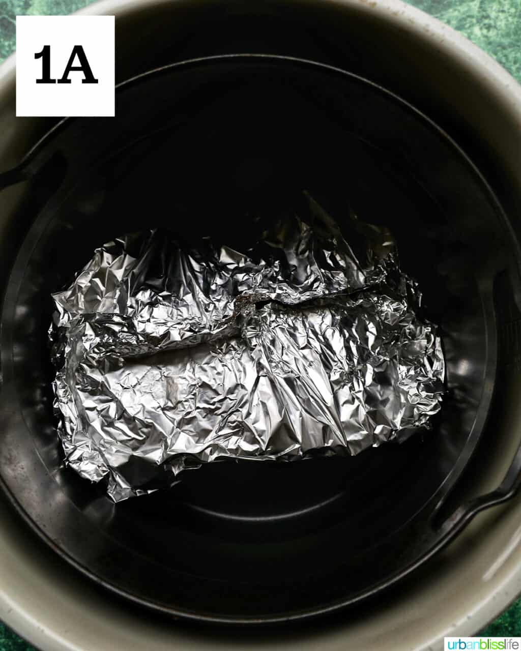 aluminum foil-wrapped ham in an air fryer basket.