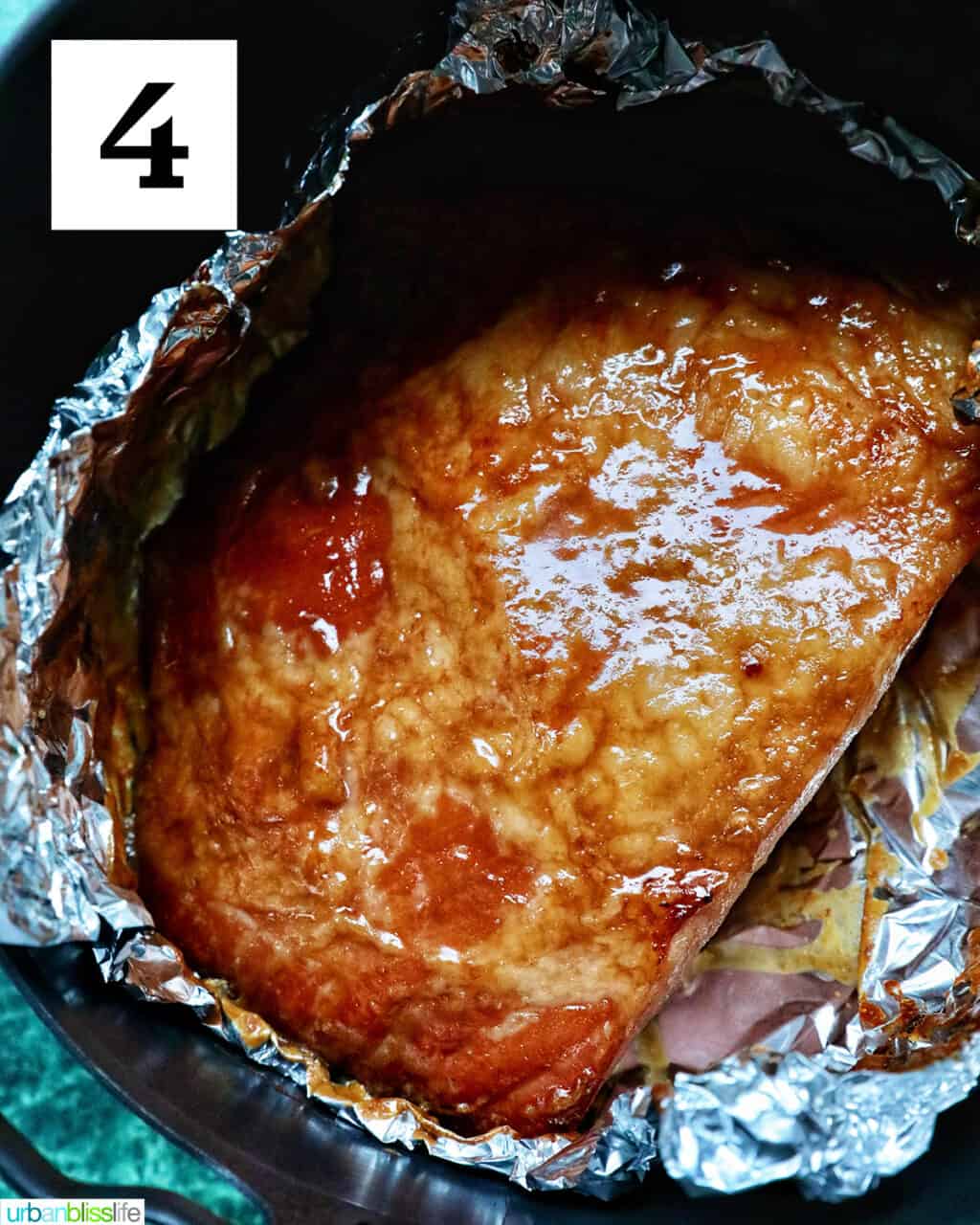 glossy glazed ham in aluminum foil in an air fryer basket.