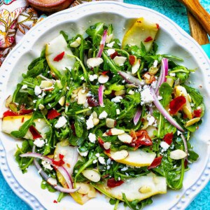 arugula, pears, prosciutto, and red onion salad in a white bowl.